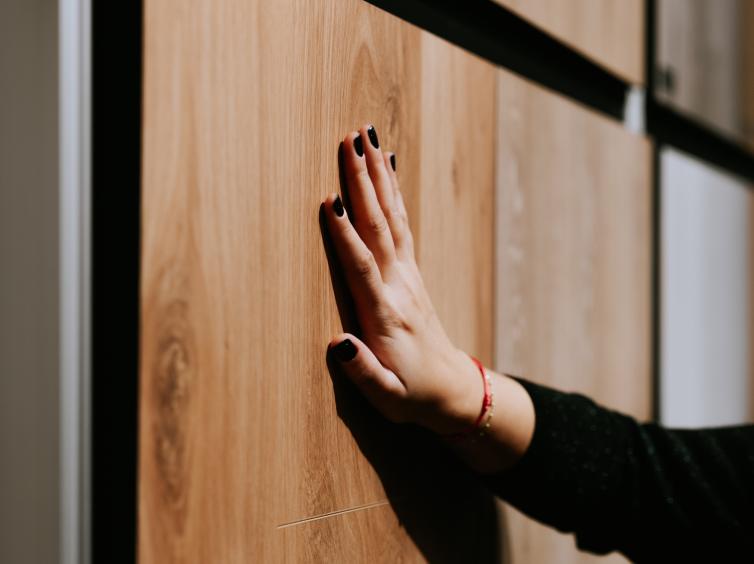 Une main posée sur une surface en bois, avec ongles vernis noir et bracelet fin rouge.