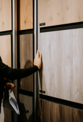 Une personne touchant un échantillon de panneau en bois sur un présentoir, tenant des documents dans l’autre main.