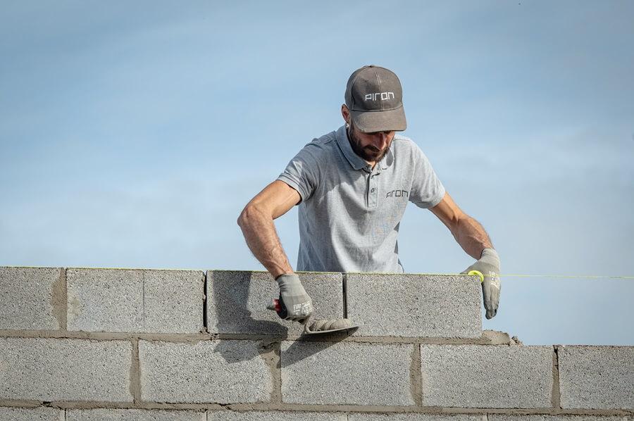 Un maçon en tenue de travail Piron Construction posant des blocs de béton avec une truelle, alignés à l’aide d’un cordeau.