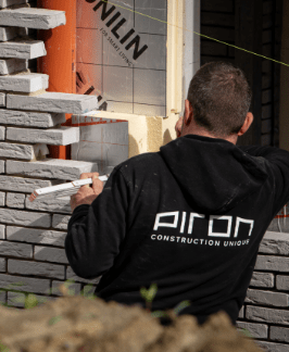 Un ouvrier de Piron Construction posant des briquettes de parement sur une façade, vêtu d’un sweat à capuche siglé de l’entreprise.