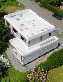 Une maison contemporaine en construction avec structure en béton brut et toit plat, vue aérienne du chantier.